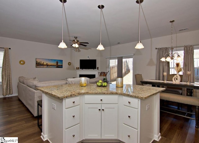 kitchen with white cabinetry, a kitchen island, light stone countertops, and hanging light fixtures