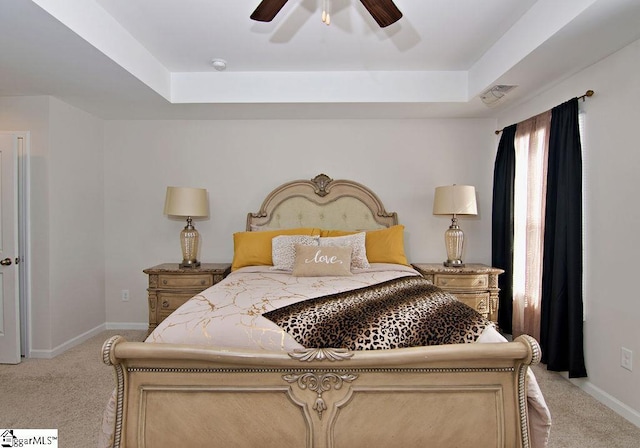 carpeted bedroom with a raised ceiling and ceiling fan