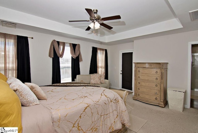 bedroom featuring ceiling fan, a tray ceiling, and light carpet