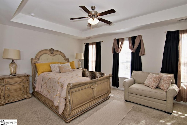 bedroom with ceiling fan, light colored carpet, and a raised ceiling