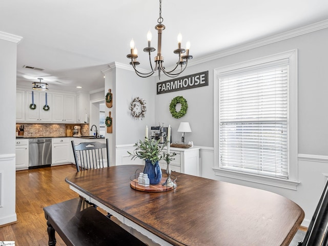 dining space featuring ornamental molding, wood-type flooring, sink, and a chandelier