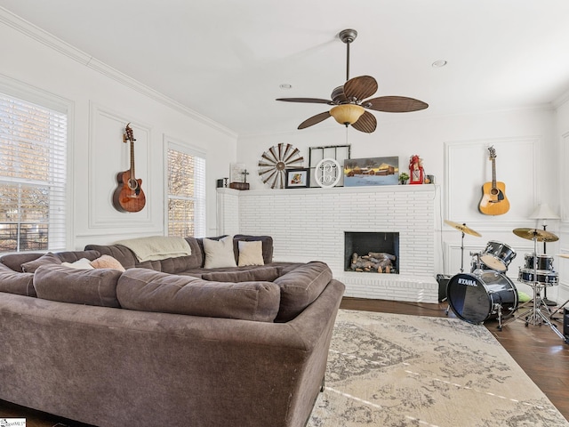 living room with dark wood-type flooring, ceiling fan, ornamental molding, and a fireplace