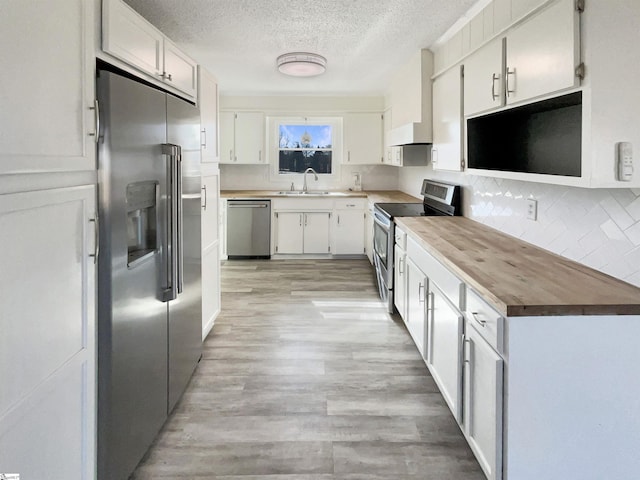 kitchen with white cabinetry, stainless steel appliances, sink, and wall chimney range hood