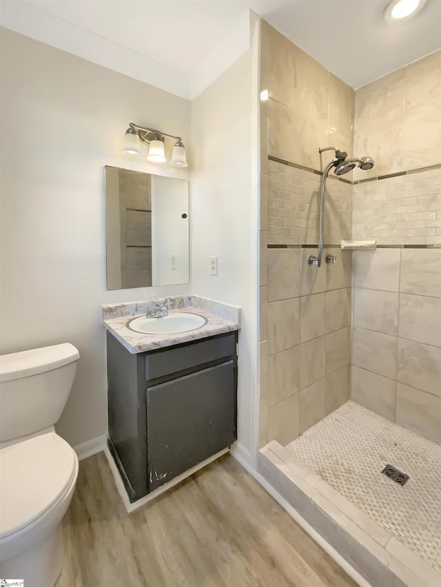 bathroom with a tile shower, hardwood / wood-style flooring, vanity, ornamental molding, and toilet