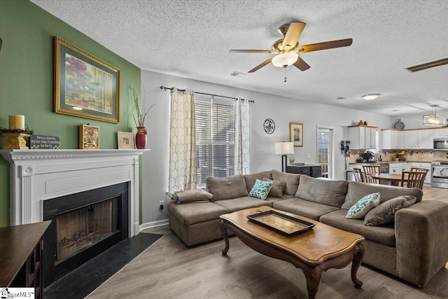 living room featuring ceiling fan, a textured ceiling, and light wood-type flooring