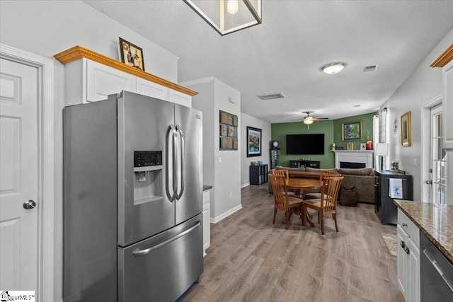 kitchen with light wood-type flooring, white cabinets, stainless steel appliances, light stone countertops, and a textured ceiling