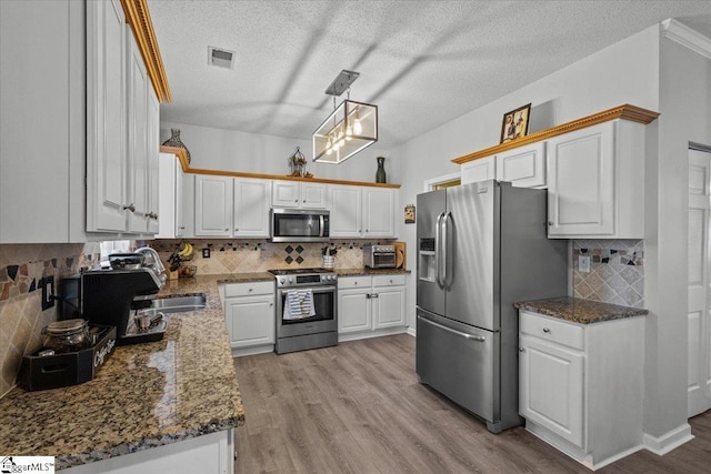 kitchen with sink, white cabinets, hanging light fixtures, stainless steel appliances, and light wood-type flooring