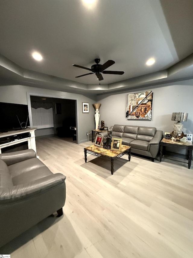 living room with ceiling fan, a tray ceiling, and light hardwood / wood-style floors