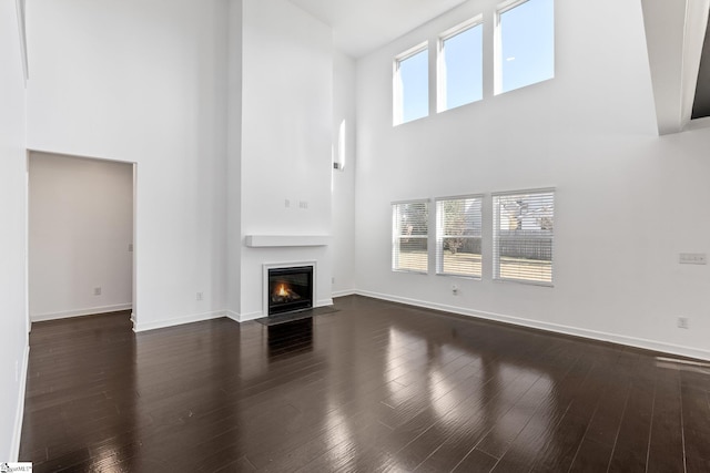 unfurnished living room with a towering ceiling, dark hardwood / wood-style floors, and a healthy amount of sunlight