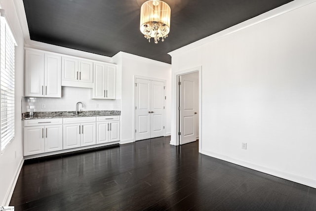 kitchen with white cabinetry, sink, light stone counters, and a notable chandelier