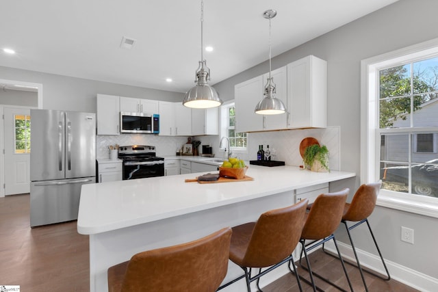 kitchen with stainless steel appliances, a kitchen bar, kitchen peninsula, and white cabinets