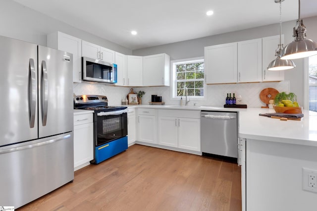 kitchen featuring white cabinetry, sink, hanging light fixtures, stainless steel appliances, and light wood-type flooring