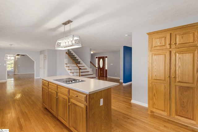 kitchen featuring light hardwood / wood-style floors, a textured ceiling, a kitchen island, black electric cooktop, and decorative light fixtures