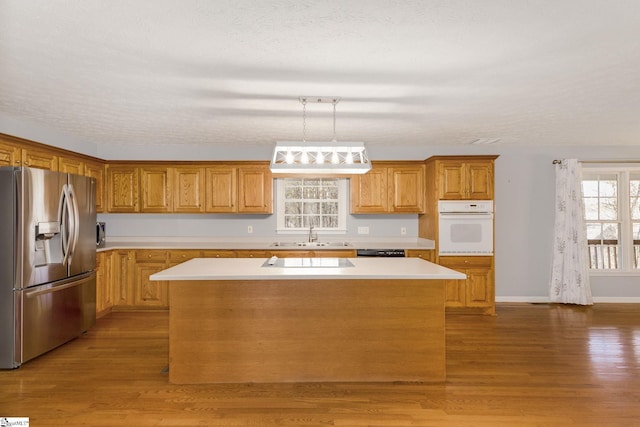 kitchen with a textured ceiling, a kitchen island, pendant lighting, light hardwood / wood-style floors, and black appliances