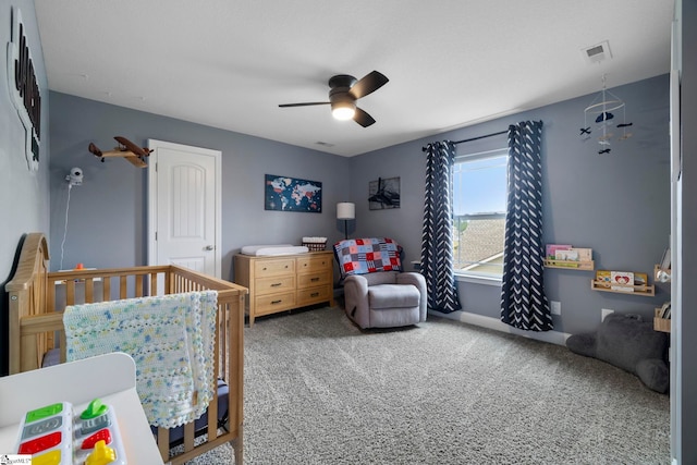 carpeted bedroom featuring ceiling fan and a crib