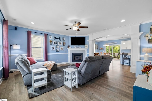 living room featuring decorative columns, ornamental molding, hardwood / wood-style flooring, and a tile fireplace