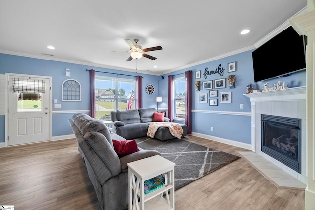 living room featuring wood-type flooring, ornamental molding, ceiling fan, and a fireplace