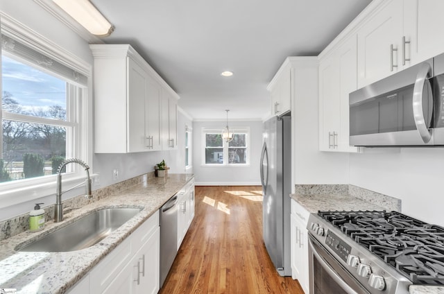 kitchen featuring sink, hanging light fixtures, stainless steel appliances, light hardwood / wood-style floors, and white cabinets