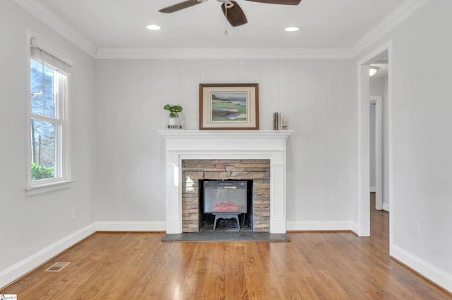 unfurnished living room featuring hardwood / wood-style floors, a stone fireplace, ornamental molding, and ceiling fan