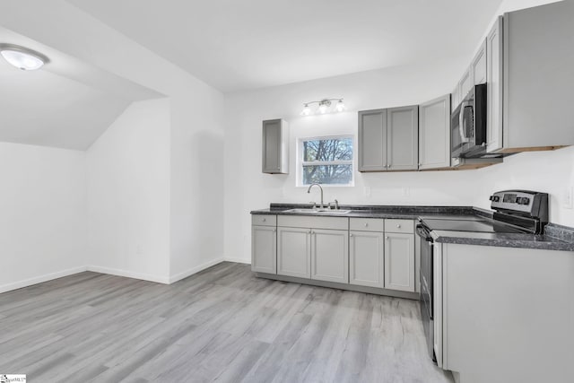 kitchen featuring lofted ceiling, sink, light hardwood / wood-style flooring, gray cabinets, and appliances with stainless steel finishes