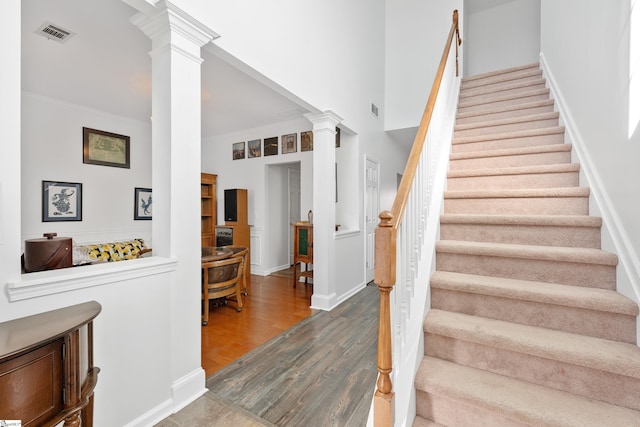 stairs with decorative columns, crown molding, and hardwood / wood-style flooring