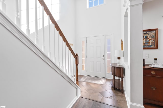 entrance foyer featuring a towering ceiling, dark tile patterned flooring, and decorative columns