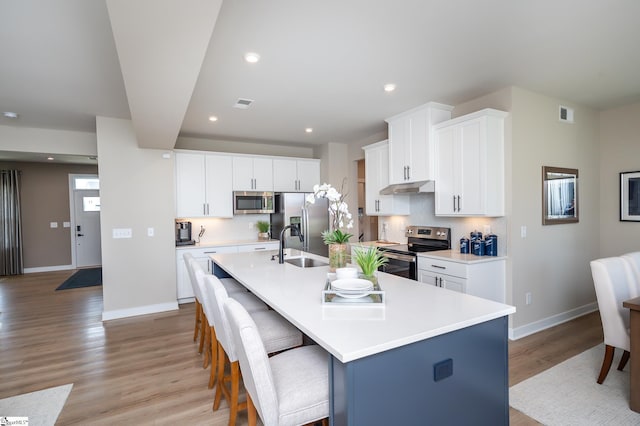 kitchen featuring a kitchen island with sink, white cabinetry, a breakfast bar, and appliances with stainless steel finishes