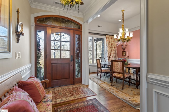 foyer with an inviting chandelier, hardwood / wood-style floors, and ornamental molding