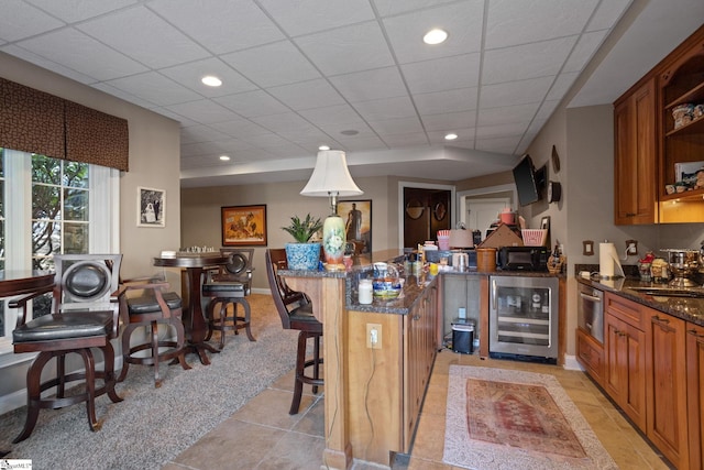 kitchen featuring wine cooler, a kitchen breakfast bar, dark stone counters, hanging light fixtures, and light tile patterned floors