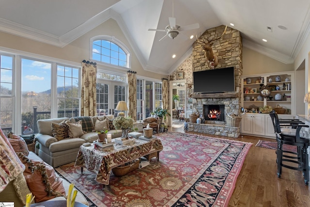 living room featuring crown molding, dark wood-type flooring, ceiling fan, high vaulted ceiling, and a stone fireplace