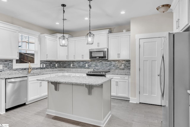 kitchen featuring a kitchen island, decorative light fixtures, white cabinetry, stainless steel appliances, and light stone countertops