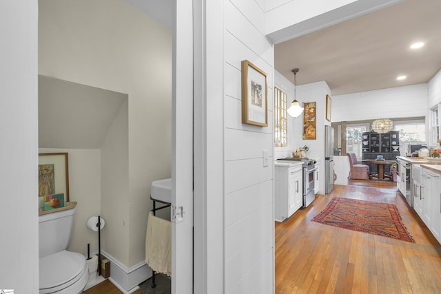 kitchen featuring stainless steel appliances, white cabinetry, hanging light fixtures, and light wood-type flooring