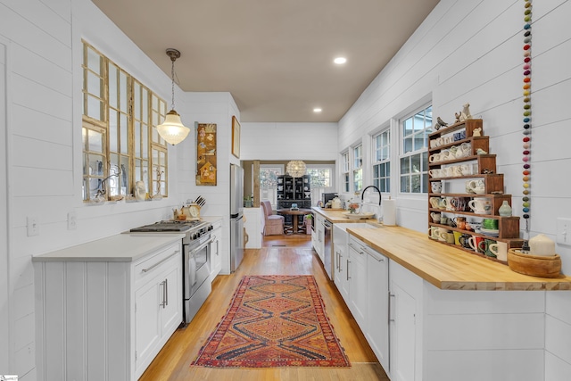 kitchen with appliances with stainless steel finishes, white cabinetry, hanging light fixtures, wood counters, and light wood-type flooring