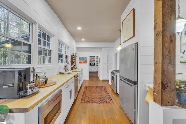 kitchen featuring hanging light fixtures, appliances with stainless steel finishes, white cabinets, and butcher block countertops