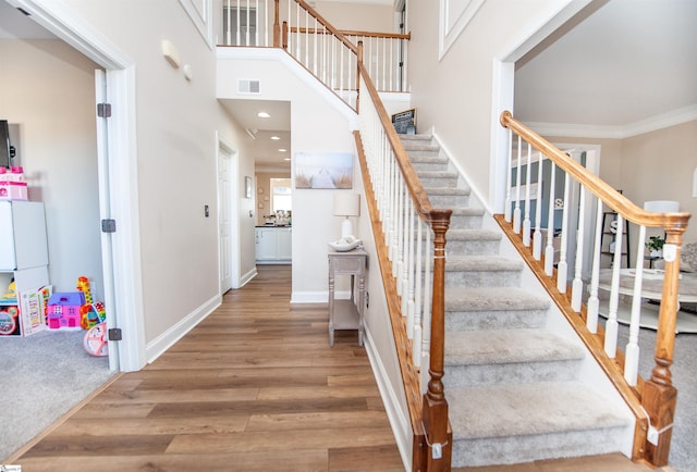 stairs featuring crown molding, hardwood / wood-style floors, and a towering ceiling