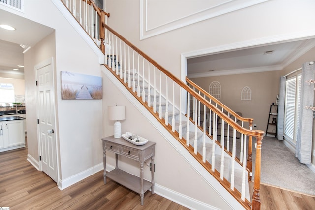 stairway with wood-type flooring, a healthy amount of sunlight, sink, and crown molding