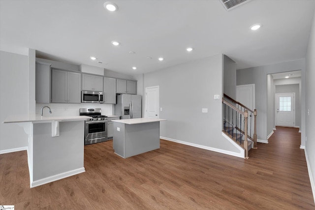 kitchen with gray cabinets, appliances with stainless steel finishes, a kitchen bar, wood-type flooring, and a kitchen island