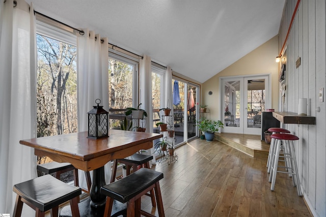 dining room featuring lofted ceiling, french doors, wood walls, and light wood-type flooring