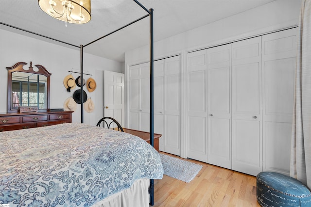 bedroom with two closets, a chandelier, and light wood-type flooring