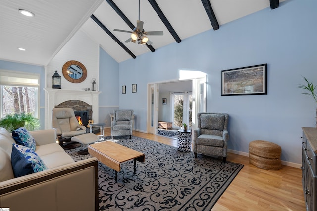 living room featuring beam ceiling, high vaulted ceiling, light hardwood / wood-style flooring, ceiling fan, and a fireplace