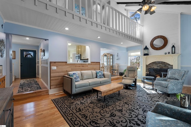 living room featuring wooden walls, a large fireplace, ceiling fan, crown molding, and light hardwood / wood-style flooring