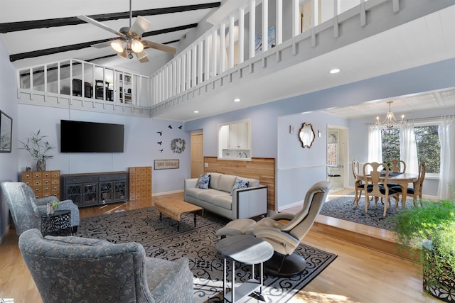 living room featuring ceiling fan with notable chandelier, wood-type flooring, beamed ceiling, and a towering ceiling