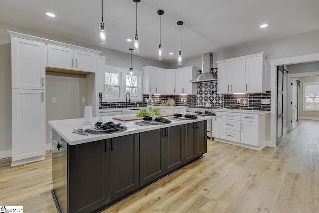 kitchen with pendant lighting, white cabinetry, decorative backsplash, a center island, and wall chimney range hood