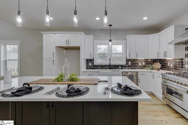 kitchen with a kitchen island, appliances with stainless steel finishes, decorative light fixtures, white cabinets, and light wood-type flooring