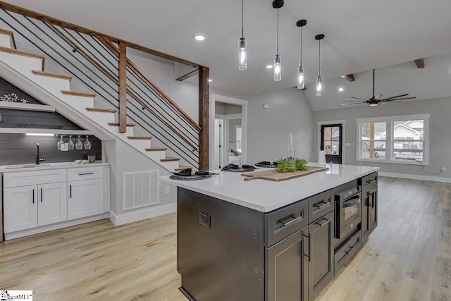 kitchen with sink, white cabinetry, a kitchen island, pendant lighting, and light hardwood / wood-style floors