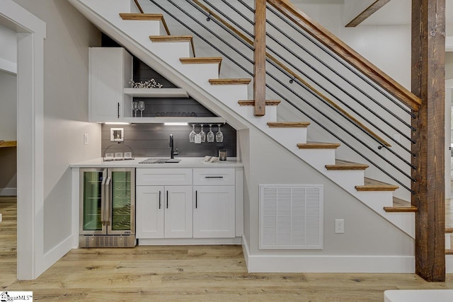 bar with sink, white cabinets, beverage cooler, decorative backsplash, and light wood-type flooring