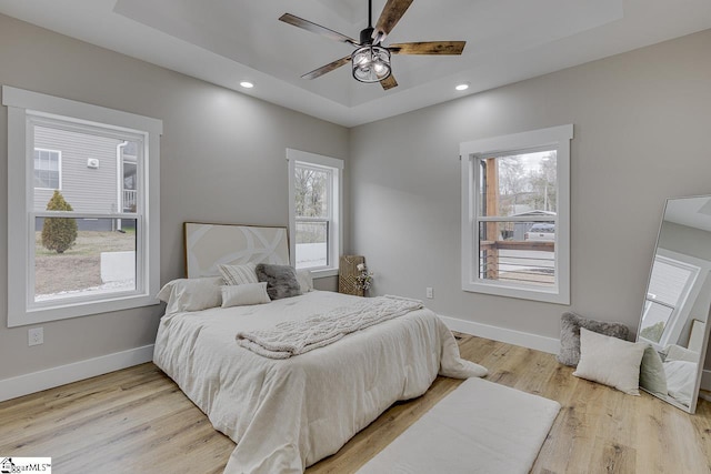 bedroom with ceiling fan, a tray ceiling, and light hardwood / wood-style floors