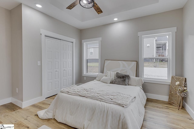 bedroom with a tray ceiling, a closet, ceiling fan, and light wood-type flooring