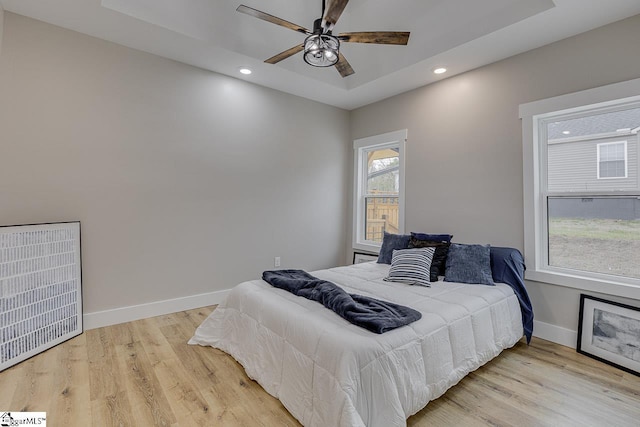 bedroom featuring ceiling fan, a tray ceiling, and light hardwood / wood-style floors