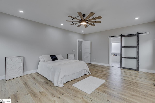 bedroom featuring light hardwood / wood-style floors, a barn door, and ceiling fan